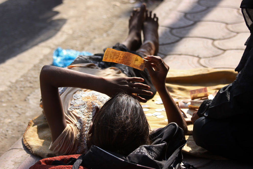 girl lies on pavement holding a ten rupee note