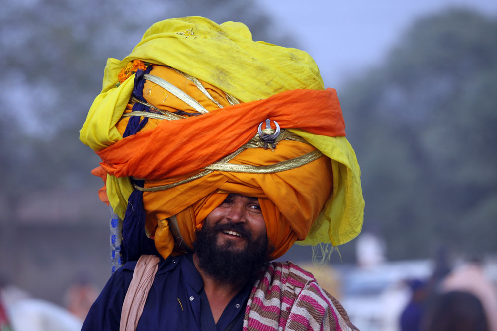 An Indian 'Nihang' or a man whose ancestors belonged to Sikh warrior clan, smiles supporting an over-sized turban as he takes part in a religious procession called Mohalla in Amritsar, India, 14 November 2012. The procession is carried out a day after the Diwali festival to mark the Bandi Chorh Diwas the day when Guru Hargobind the sixth Guru or the Master of the Sikhs reached Amritsar after his release from Gwalior fort during the reign of Mughal emperor Jahangir. Each year members of various major Nihang groups display their martial arts and horse riding skills during the Mohalla procession.