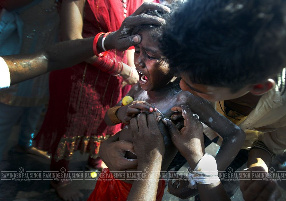 A child cries in pain as a needle is pierced through his skin as a ritual for a religious ceremony