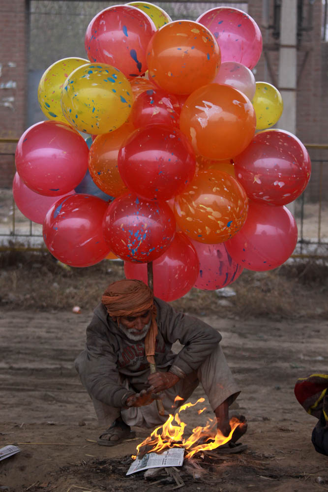 balloon vendor warms himself near a fire on a roadside on a very cold day in Amritsar