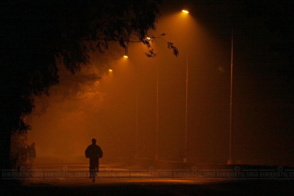 man rides cycle on foggy road with orange street light