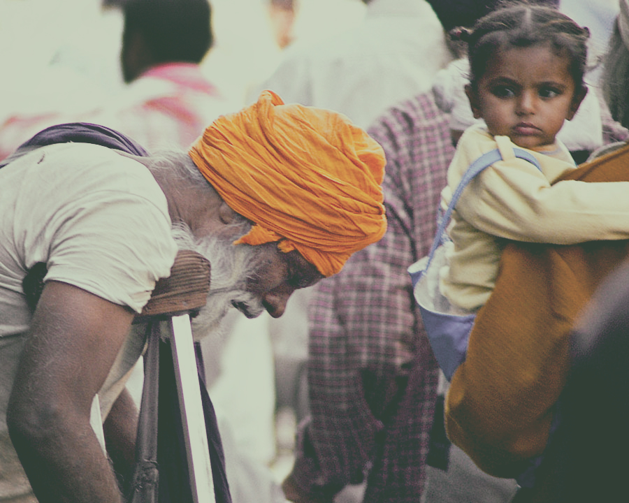 a child looks at a physically challenged man with his head down holding crutches