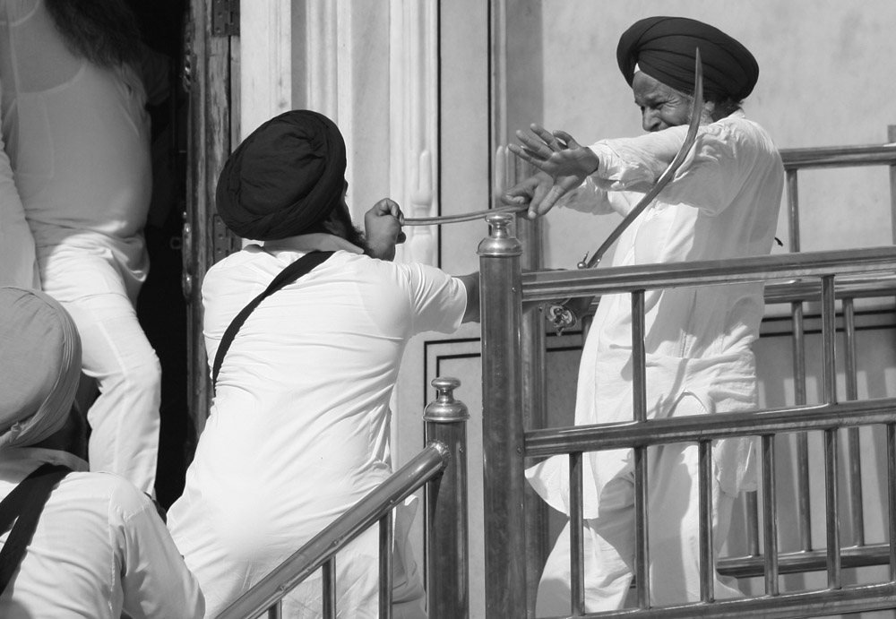 Sikh men fight with swords at the golden temple