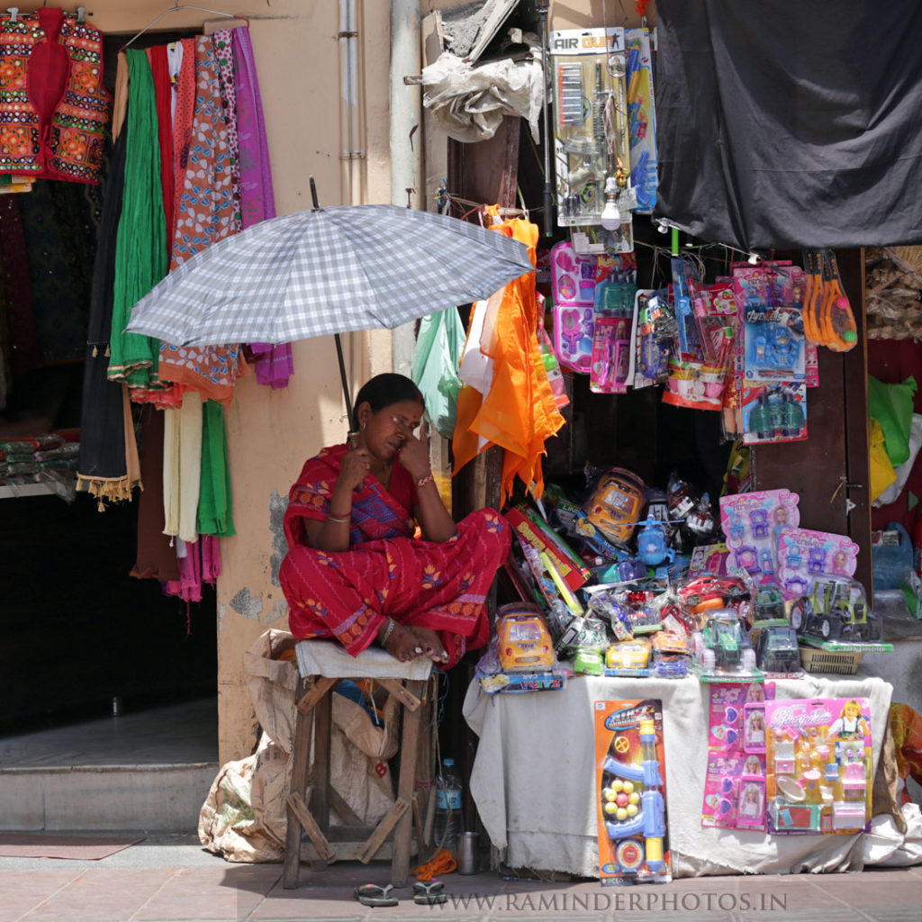 vendor holds umbrella and waits for customers on a hot day
