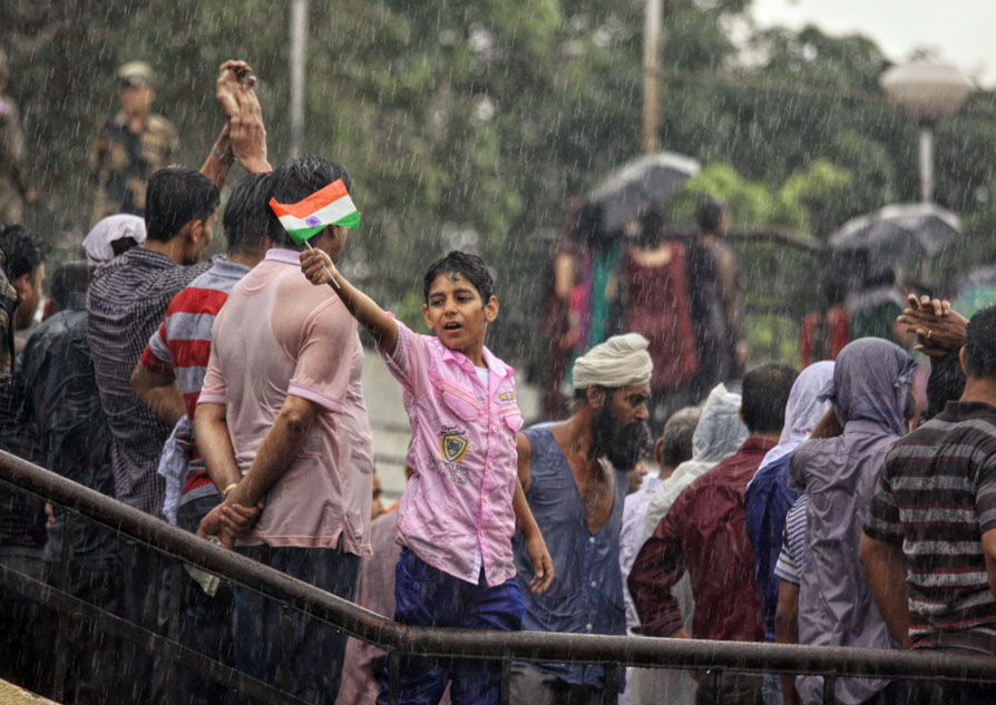 A young boy waves an Indian flag in rain as people stand nearby