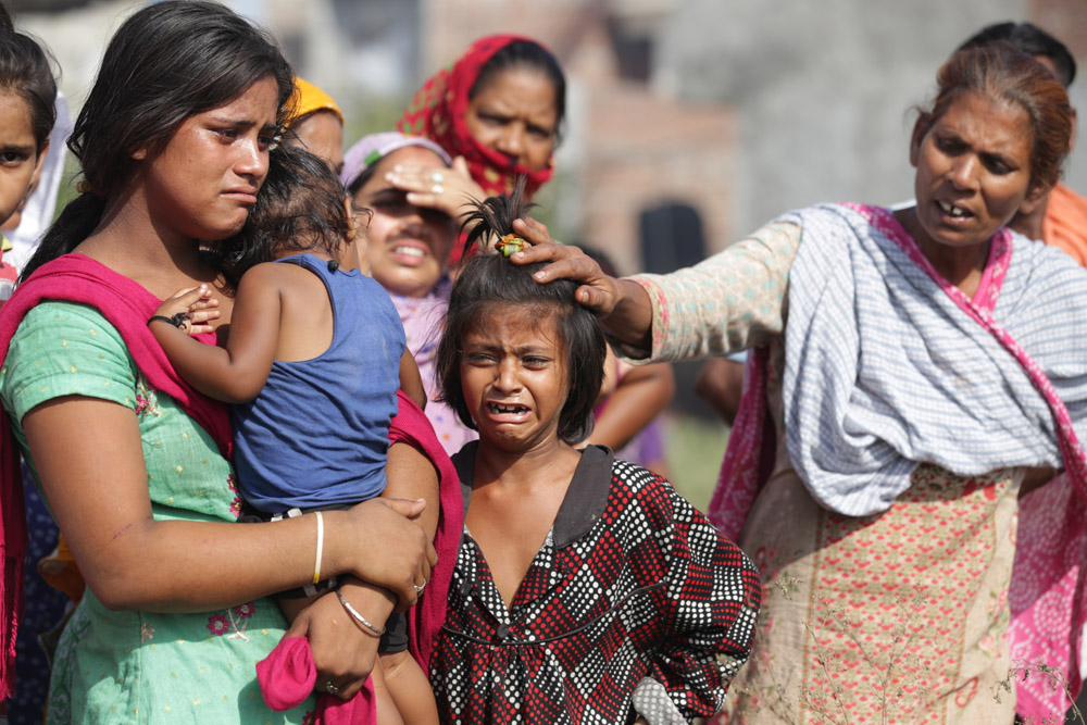 A child is comforted by a woman while she cries after their house got burnt in fire her mother stands nearby