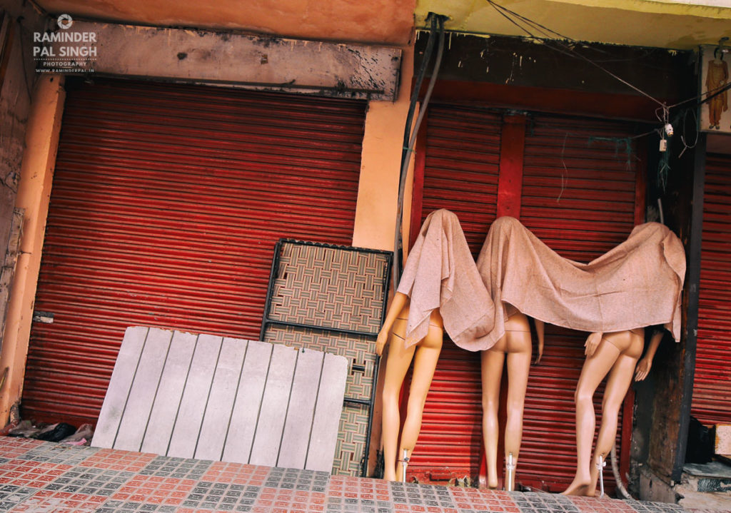 Partially covered mannequins outside closed red-shuttered shops in Amritsar, India.