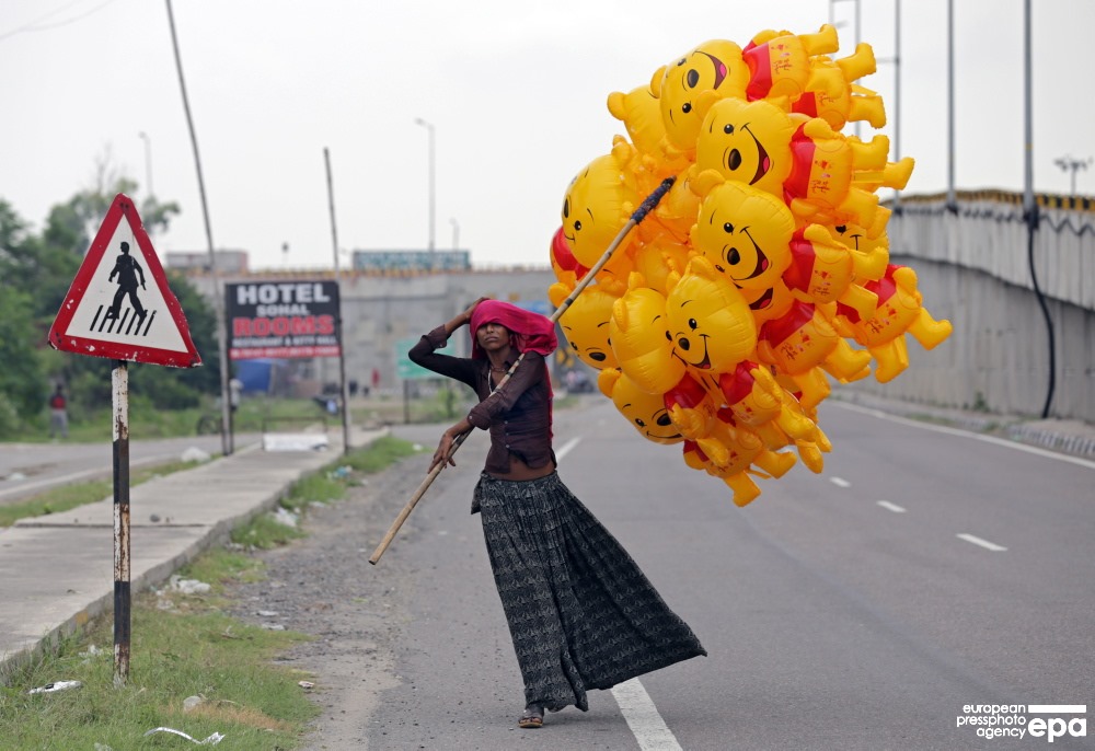 A young nomad woman sells yellow colored Winnie-the-pooh shaped balloons on a highway and adjusts her head scarf due to wind in Amritsar